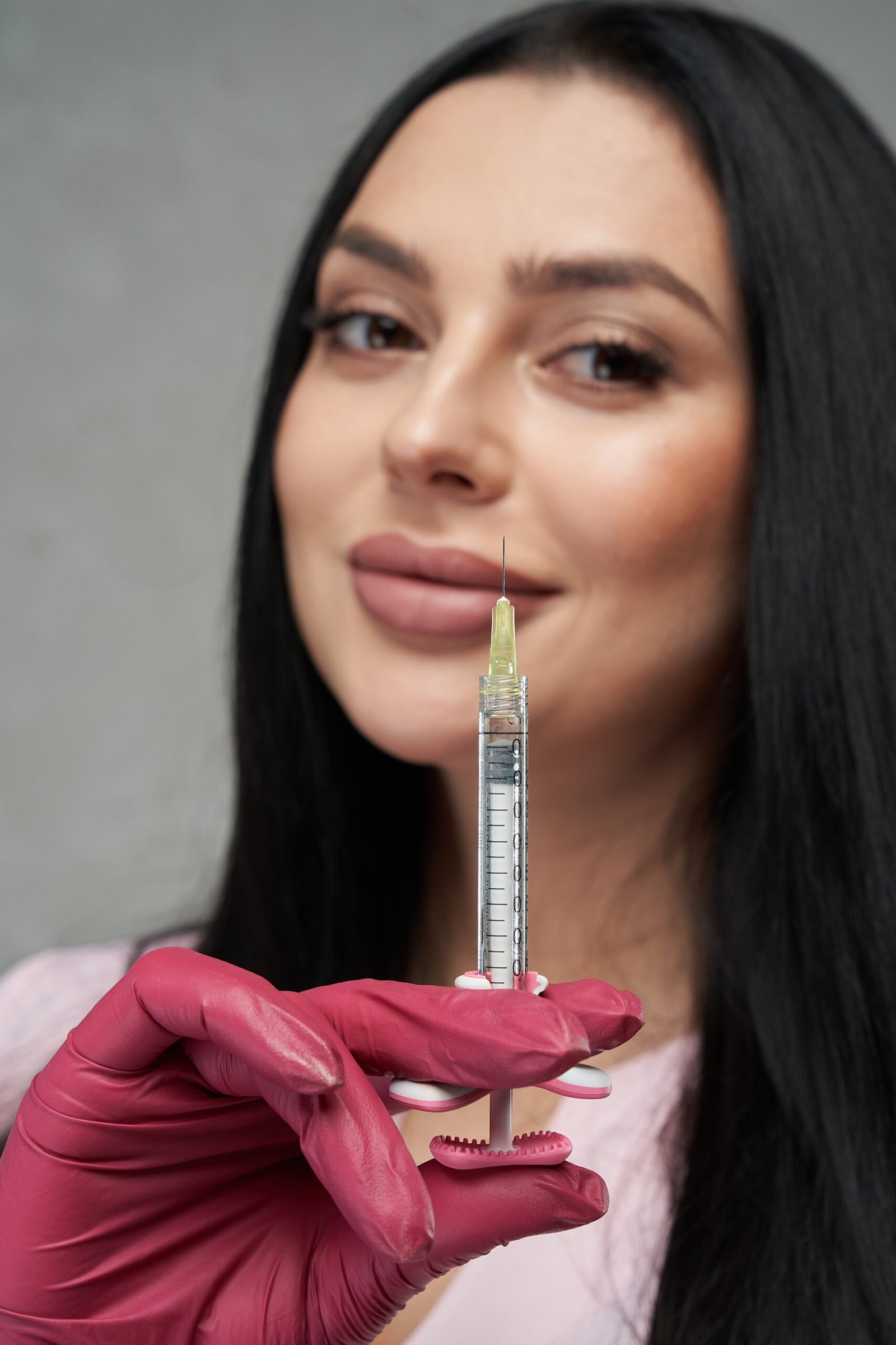 beautiful female wearing pink gloves showing filled syringe camera close up portrait scaled