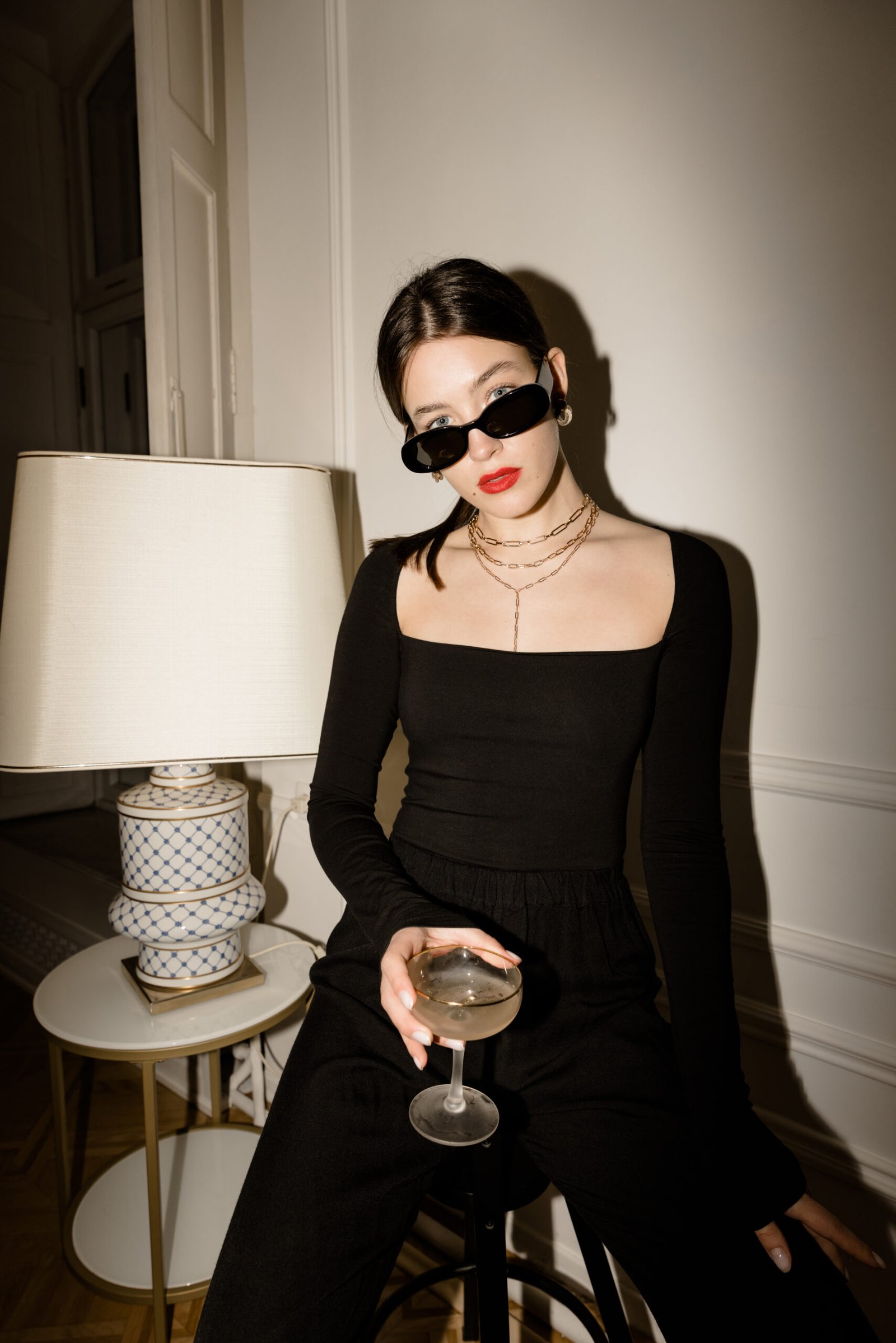 fashionable young caucasian woman black glasses clothes looks camera sitting indoors with glass booze stylish lady having good time scaled