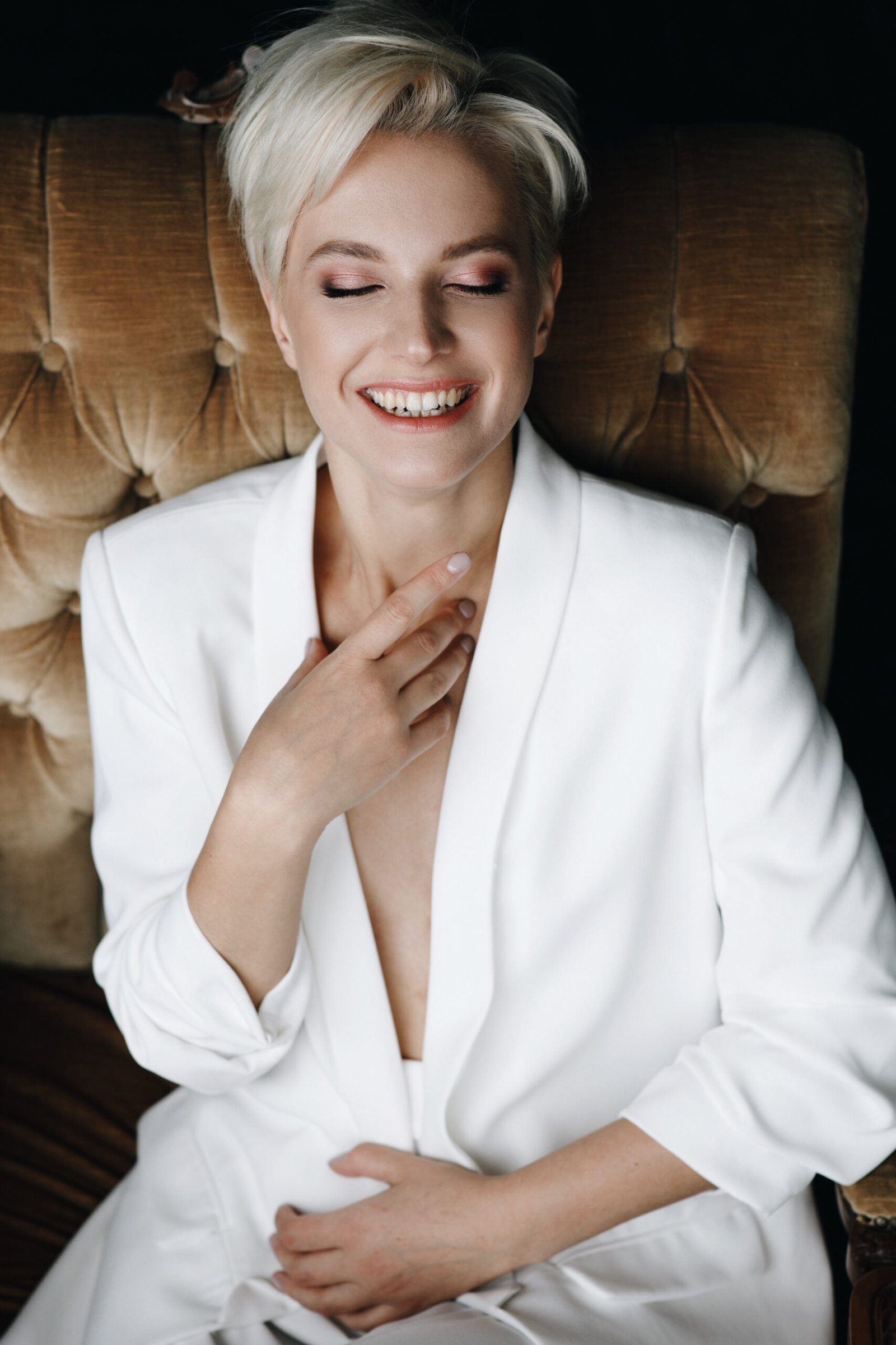 gorgeous smiling blonde fashion model sits white suit soft armchair scaled