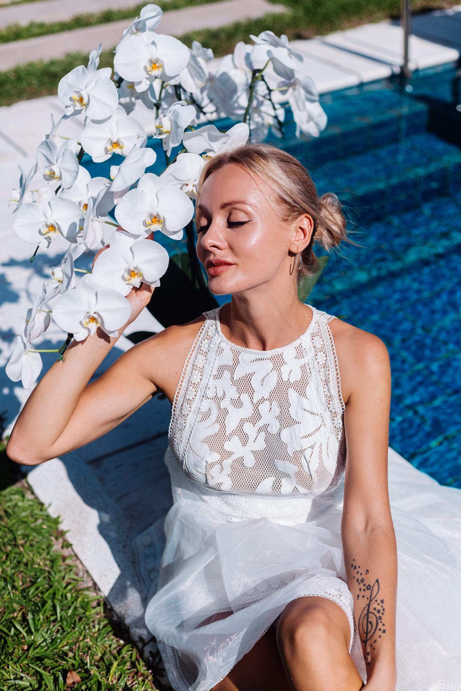 outdoor portrait woman white wedding dress sitting near blue swimming pool with flowers scaled