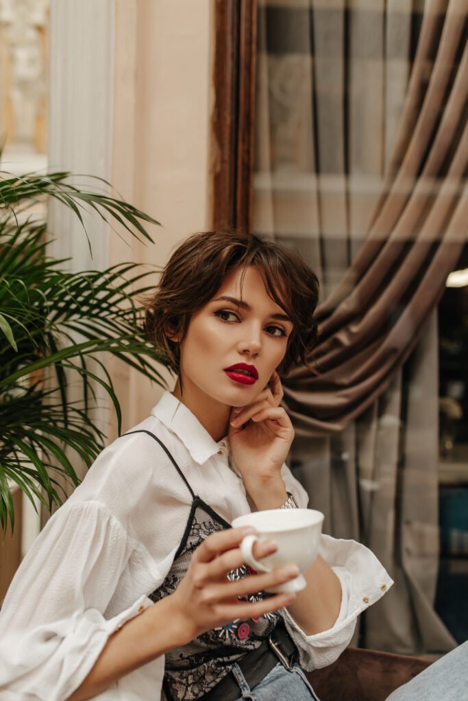 Understanding Rosacea: Causes, Triggers, and Treatment in Dubai's Heat 7 short haired woman long sleeve shirt with red lips holding cup coffee restaurant woman with brunette hairstyle poses cafe
