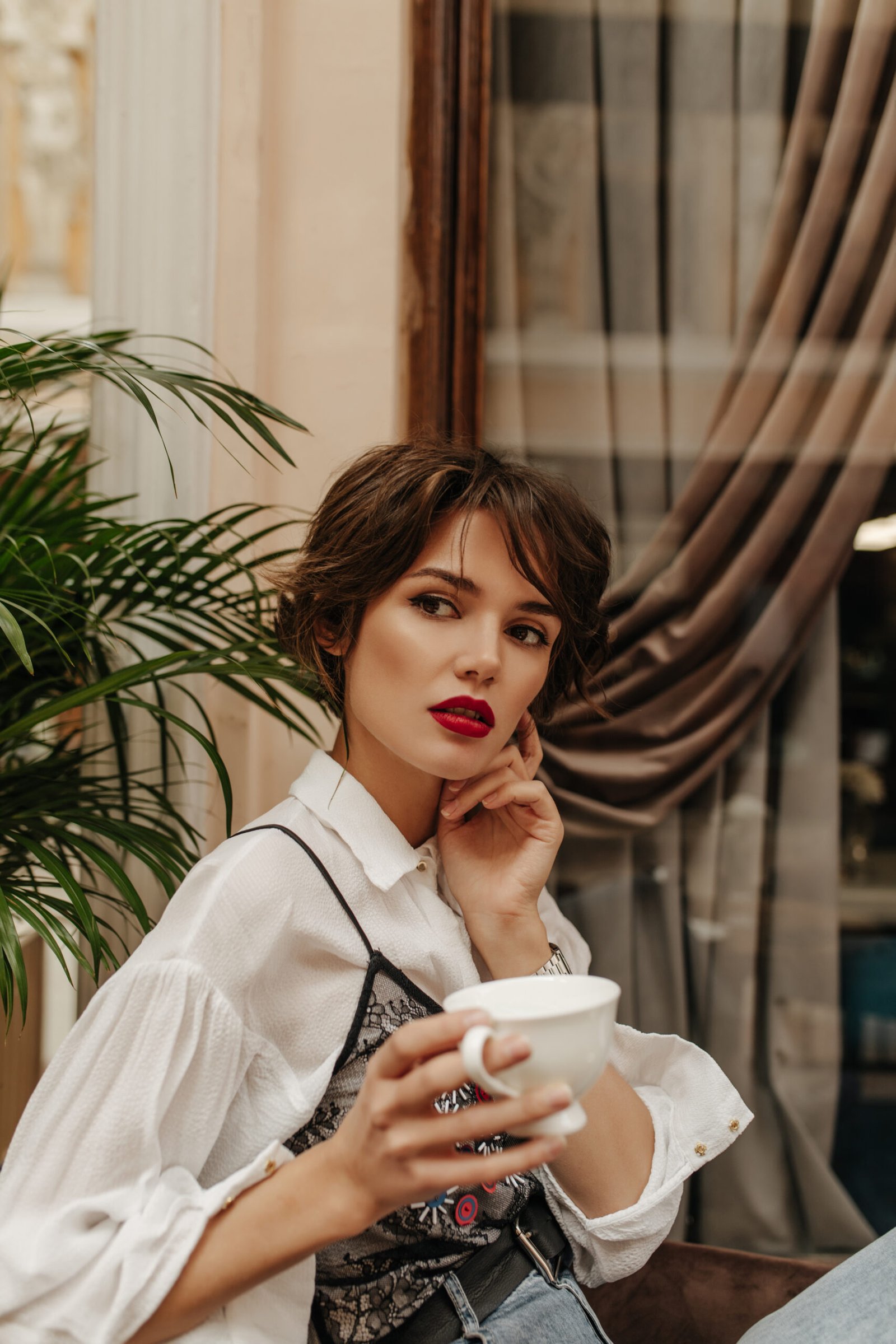 short haired woman long sleeve shirt with red lips holding cup coffee restaurant woman with brunette hairstyle poses cafe scaled